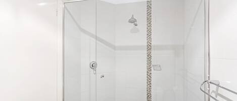 A glass-enclosed shower stall with a showerhead, a control knob, and a tiled floor.