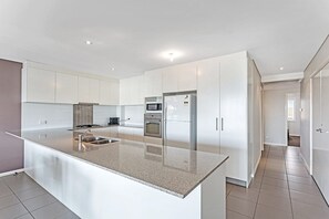 A modern kitchen with white cabinetry, a granite countertop, and stainless steel appliances including a refrigerator, oven, and microwave.