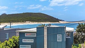A coastal view with a beach and a hill in the background. There are mobile homes in the foreground with visible windows and satellite dishes.
