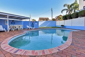 A swimming pool with a brick border, lounge chairs, and a covered seating area.