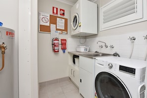 A laundry room with a front-loading washing machine, a fire extinguisher, and a fire blanket on the wall.