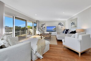 A modern living room with a large TV, comfortable seating, and a view of the outdoors.