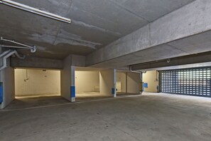 An empty parking garage with concrete walls, a garage door, and exposed pipes.