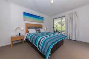 Een slaapkamer met een bed, een nachtkastje, een lamp, een schilderij en uitzicht door een glazen deur.
