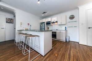 A modern kitchen with white cabinets, a central island with bar stools, a microwave, oven, and a clock on the wall.