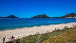 Uma praia com águas azul-claras, areal arenoso e montanhas ao longe.