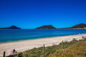 Een strand met helderblauw water, een zandstrand en bergen in de verte.