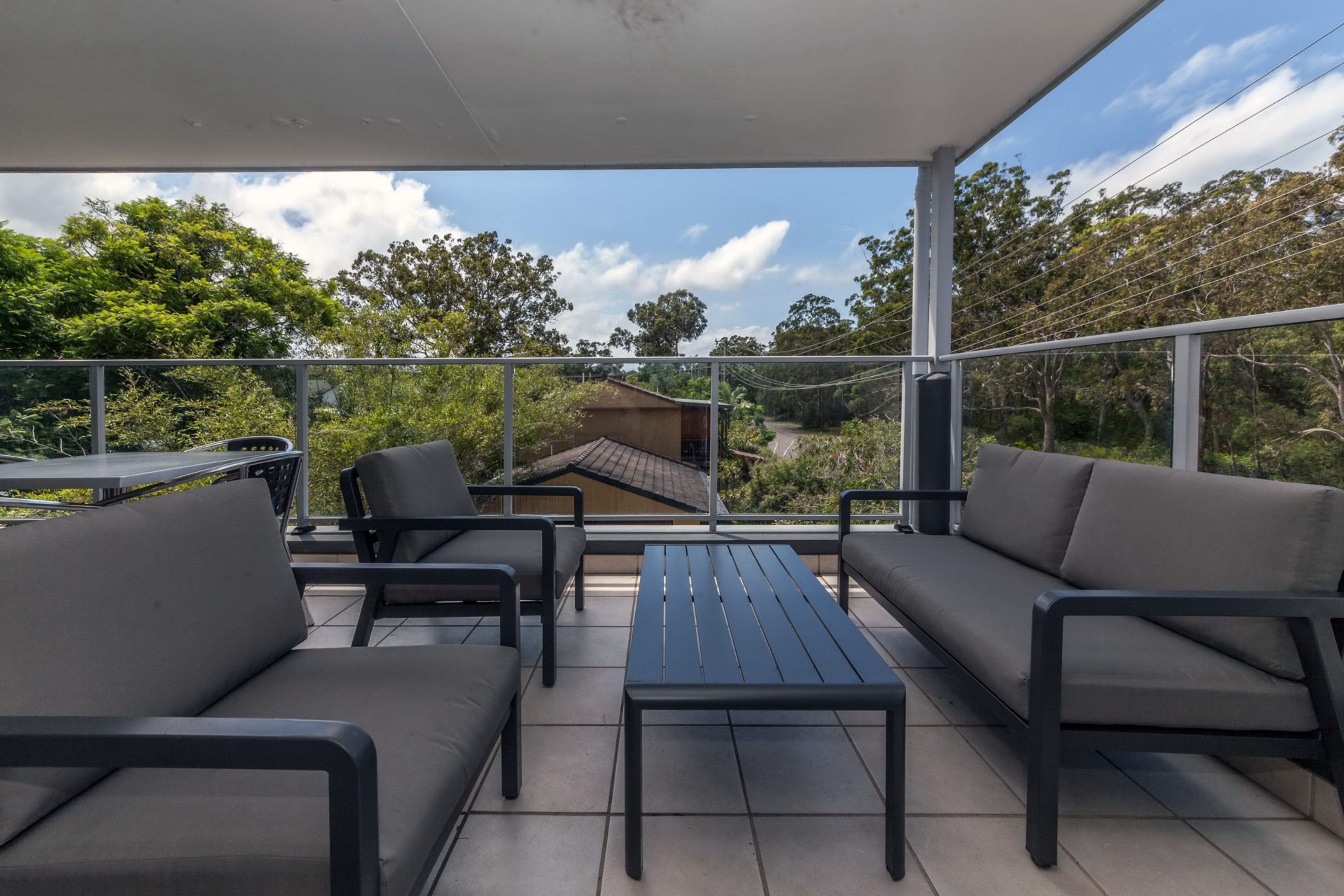 An outdoor patio with a table and chairs, a sofa, and a view of a road and trees.