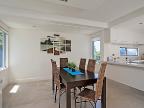 A modern kitchen with a dining area, featuring a dark wooden table, wicker chairs, and a large window.