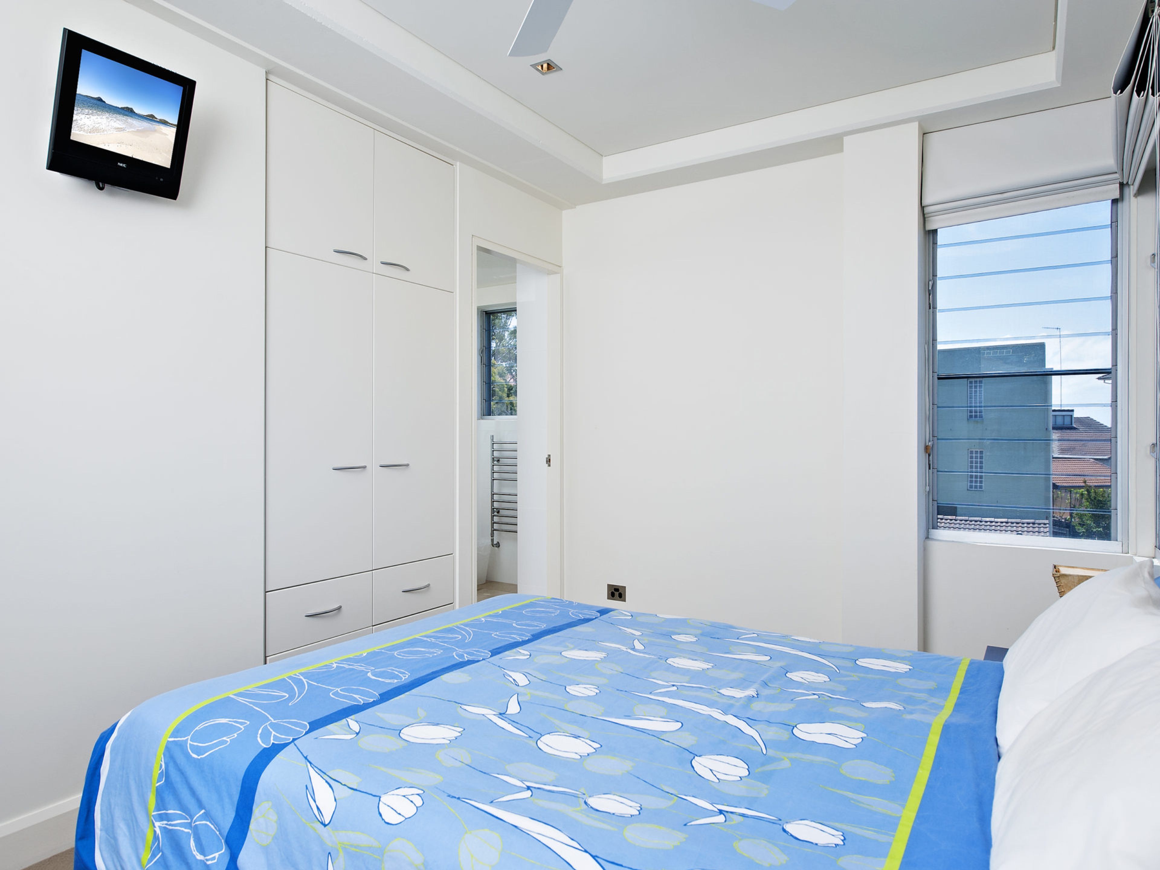 Ein Schlafzimmer mit Bett, Kleiderschrank, Fenster und einem Flachbildfernseher an der Wand.