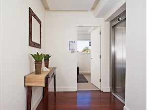 A hallway with a wooden console table, two potted plants, a mirror, and a door leading to another room.