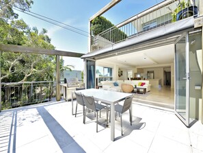 A modern outdoor patio with a dining table and chairs, a barbecue grill, and a glass door leading to an interior living space.