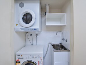 A compact laundry room with a front-loading washing machine, a small sink, and a ventilation system.