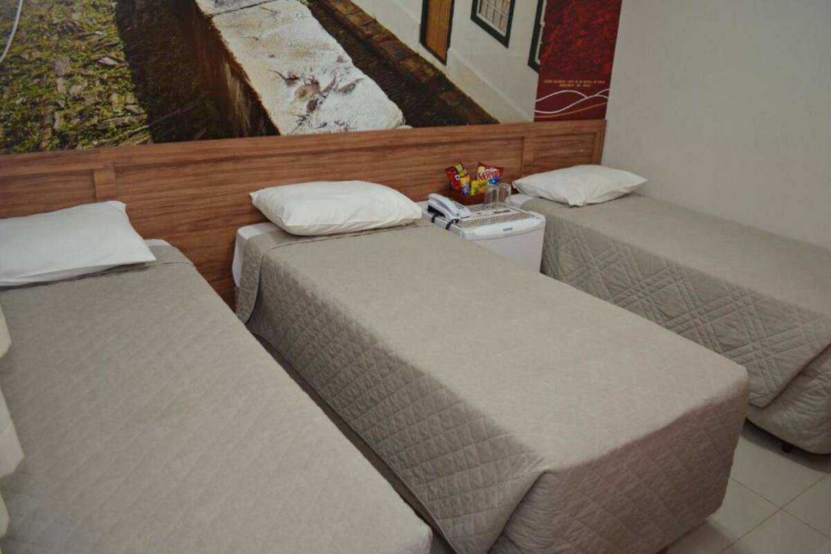 A hotel room with two single beds, a wooden headboard, and a poster on the wall.