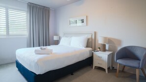 A hotel room with a bed, bedside tables, a chair, and a window with curtains. - The Helm Waterfront Apartment in Nelson Bay (Nelson Bay)