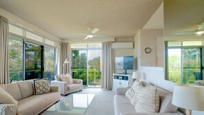 A modern living room with a flat-screen TV, two sofas, a coffee table, and a ceiling fan. - The Helm Waterfront Apartment in Nelson Bay (Nelson Bay)