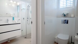 A modern bathroom with a glass shower enclosure, a white toilet, and a vanity with a mirror. - The Helm Waterfront Apartment in Nelson Bay (Nelson Bay)