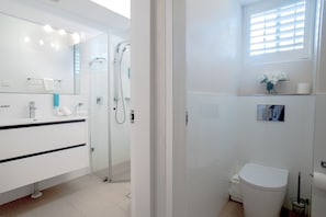 Een moderne badkamer met een glazen douchecabine, een wit toilet en een wastafel met spiegel.