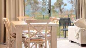 A dining area with a wooden table and chairs, a sofa, and a view through a large window. - The Helm Waterfront Apartment in Nelson Bay (Nelson Bay)