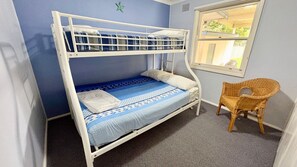 Ein Stockbett mit blauer und weißer Bettdecke, ein Korbstuhl und ein Fenster mit Blick auf Grünflächen.