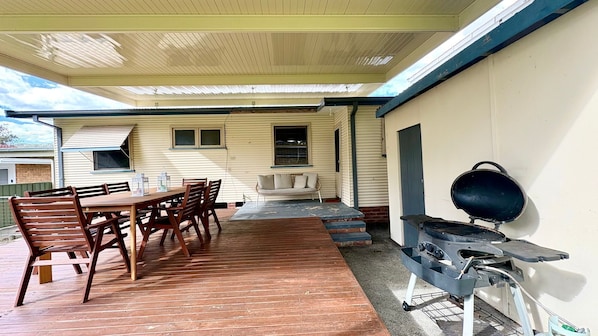Eine überdachte Terrasse mit Holztisch und -stühlen, einer Couch und einem Grill.