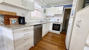 A compact kitchen with white cabinets, a dishwasher, an oven, and a coffee maker.