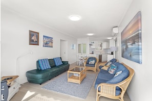 A modern living room with a green sofa, a blue sofa, and a dining area with a white table and chairs.