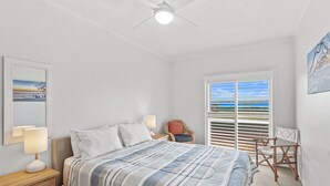 Een slaapkamer met een bed, nachtlampen, een stoel, een raam met zonwering en een plafondventilator.