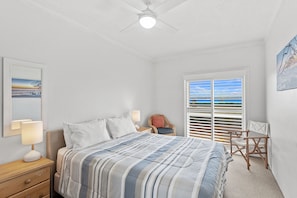 Quarto com cama, abajures, uma cadeira, janela com persianas e ventilador de teto.