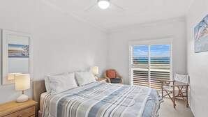 Une chambre à coucher comprenant un lit, des lampes de chevet, une chaise, un bureau, une fenêtre avec des stores et un luminaire au plafond.