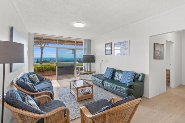 A spacious living room with a view of the sea, furnished with a sofa, chairs, and a coffee table.