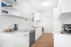 A modern kitchen with white cabinetry, a dishwasher, a sink, and a stove. - Bella Vista 22 Waterfront Apartment in Shoal Bay (Shoal Bay)