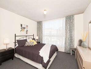 Een hotelkamer met een bed, nachtkastjes, een lamp, een raam met gordijnen en een aan de muur hangend kunstwerk.