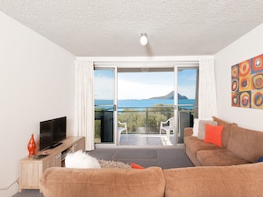 A living room with a sofa, a television, and a balcony with a view of the sea. - Ocean Shores Stunning Waterfront Nelson Bay Escape (Nelson Bay)