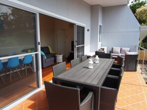 An outdoor patio with a dining table and chairs, a sofa, and a TV. - Pollys' View Nelson Bay Water View Family Home (Nelson Bay)