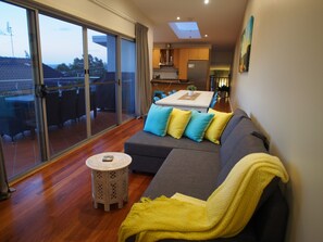 A modern living room with a grey sofa, yellow and blue cushions, a small round table, and a yellow throw blanket. - Pollys' View Nelson Bay Water View Family Home (Nelson Bay)