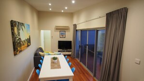 A modern living room with a dining area, a flat-screen TV, and a large window with curtains. - Pollys' View Nelson Bay Water View Family Home (Nelson Bay)