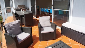 An outdoor patio with wicker furniture, a grill, and a sliding glass door leading to an indoor dining area. - Pollys' View Nelson Bay Water View Family Home (Nelson Bay)