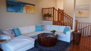 Ein Wohnzimmer mit einem weißen Ecksofa, einem Holztisch und einer Treppe mit Holzbalken.