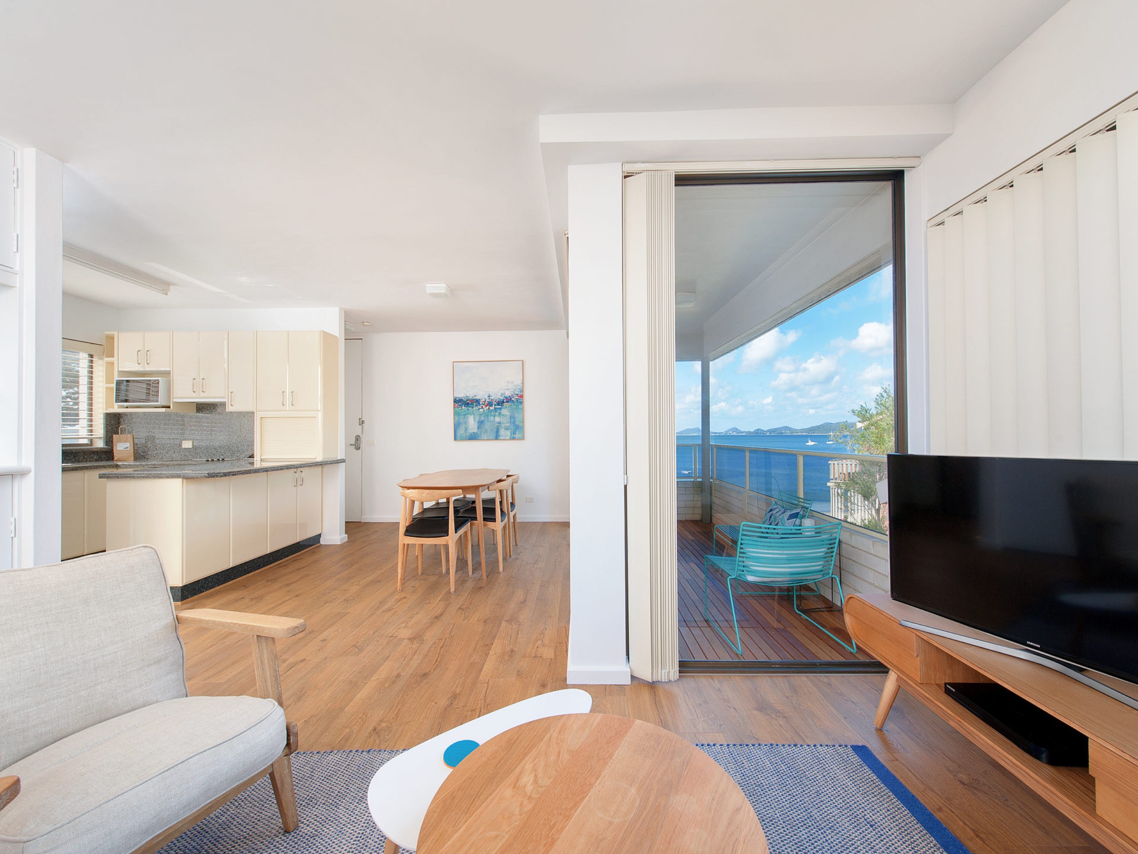 A modern living space with a kitchen, dining area, and a balcony with a TV.