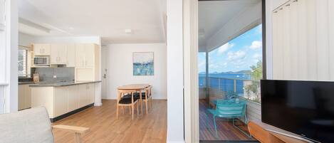A modern living space with a kitchen, dining area, and a balcony with a TV.