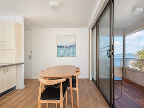 Een balkon met een houten tafel en stoelen, een glazen deur die uitkomt op een terras, en een schilderij aan de muur.