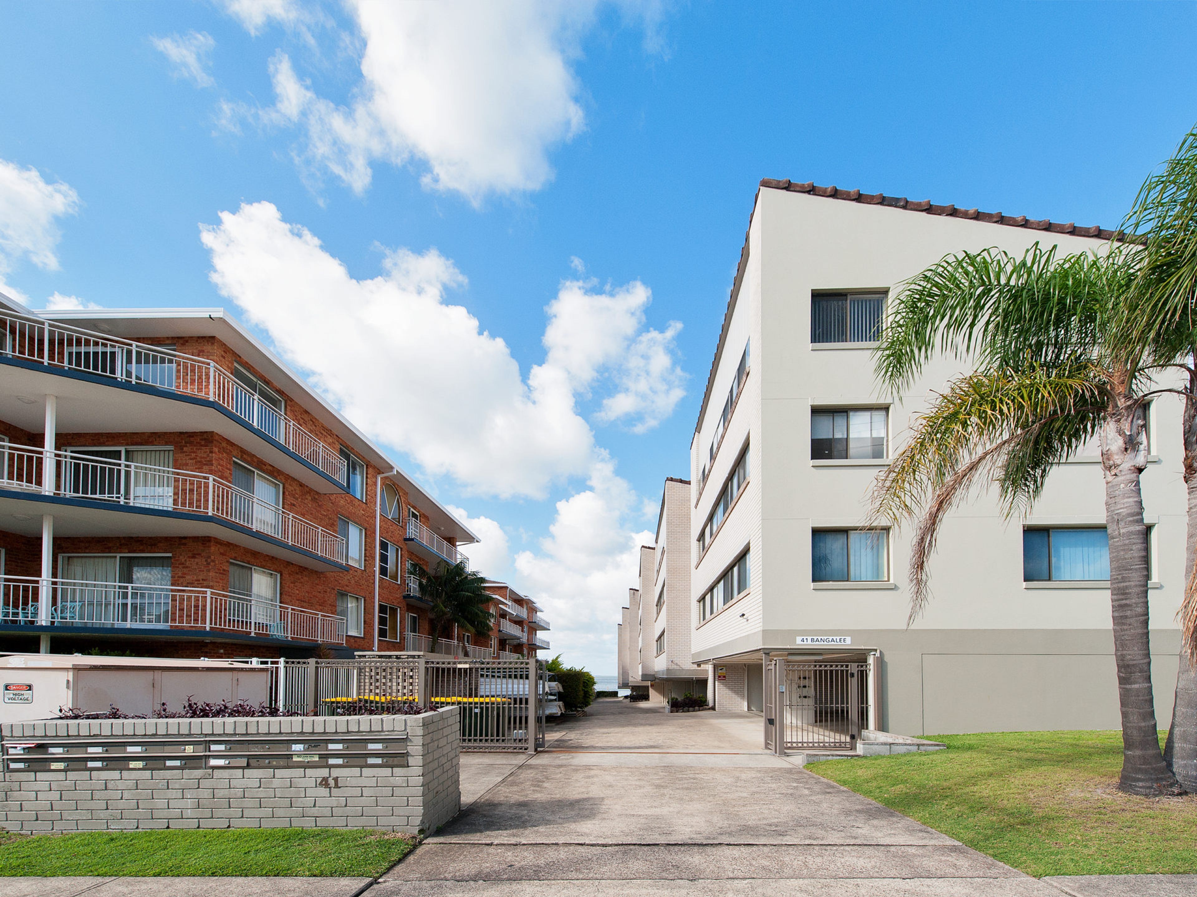 A multi-story residential building with balconies, a gated entrance, and a clear sky.