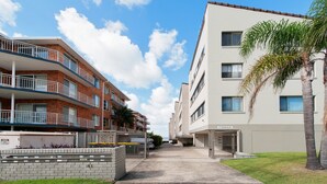 Um edifício residencial com várias andares, varandas, portão fechado e céu claro.