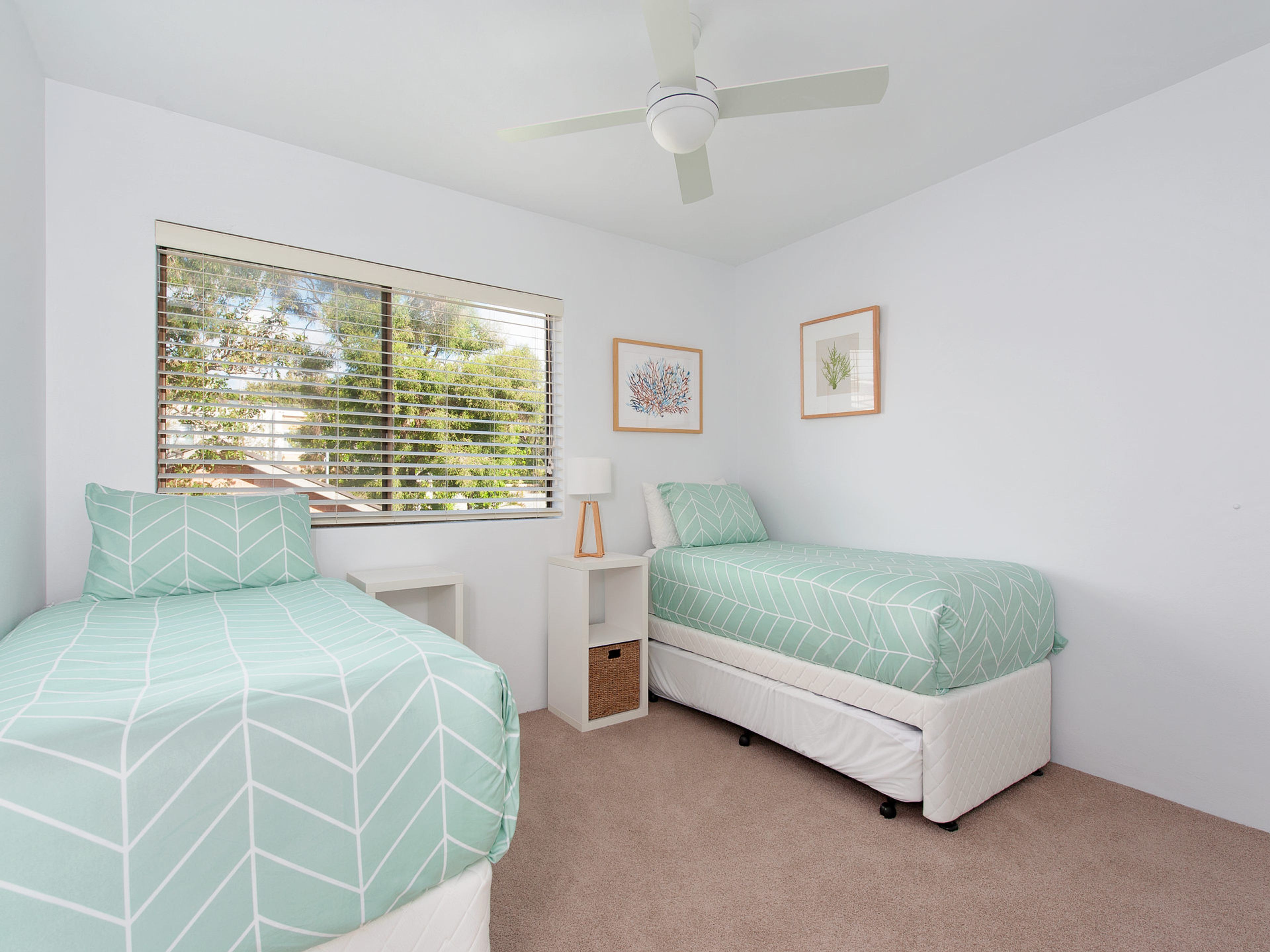 A bedroom with two beds, a ceiling fan, and a window with blinds.
