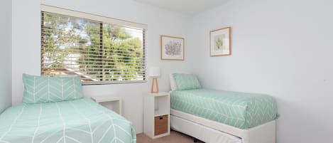 A bedroom with two beds, a ceiling fan, and a window with blinds.