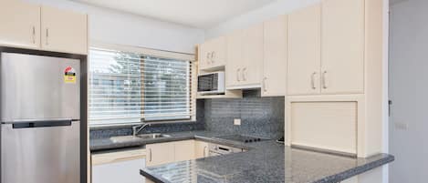 A modern kitchen with a stainless steel refrigerator, a microwave, and a granite countertop.
