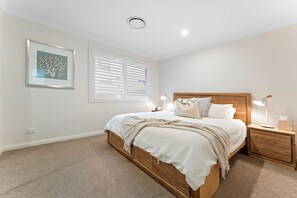 A bedroom with a wooden bed, white bedding, a nightstand with a lamp, and a framed picture on the wall. - Signature House Family Retreat Corlette (Corlette)