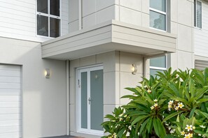 A modern two-story house with a white exterior, a garage door, and a front door with a glass panel. - Signature House Family Retreat Corlette (Corlette)