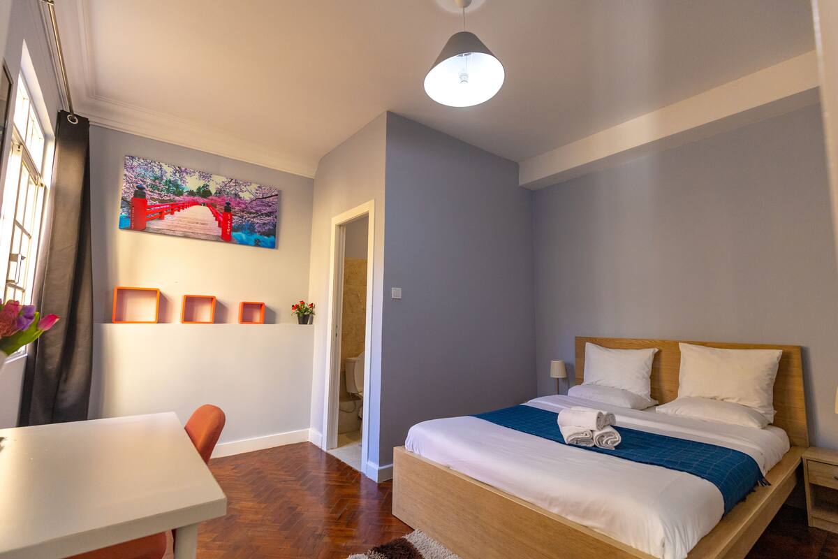 Una habitación de hotel moderna con una cama de madera, un escritorio y un cuadro de un puente.